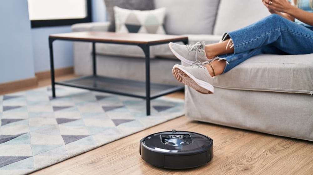 Young woman using smartphone cleaning floor using cleaner robot vacuum at home